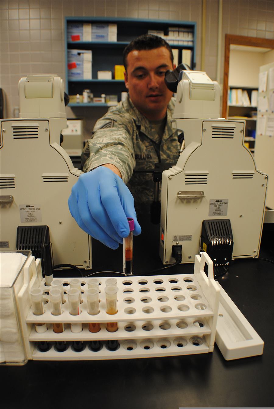Technician placing a blood sample into a test tube rack in a medical laboratory